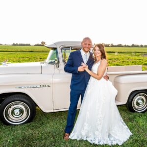 Olivia And Alex posing in front of a classic truck at the wedding